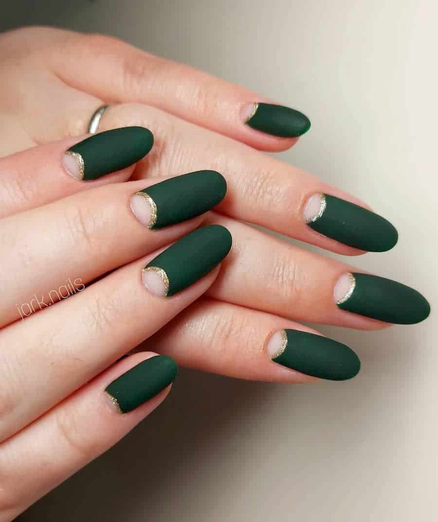 a hand with long round nails with matte dark green and ɴuᴅᴇ half moons with gold glitter borders