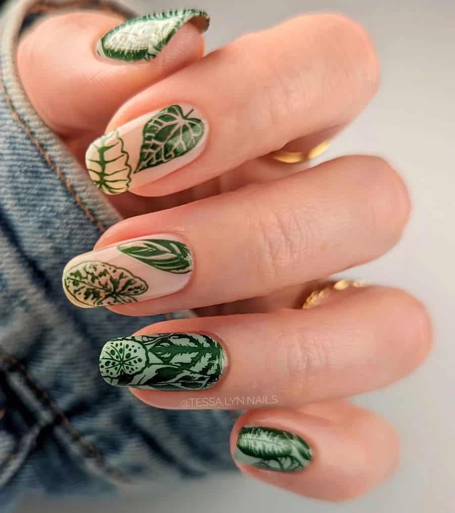 a hand with medium-length squoval nails painted light green with two ɴuᴅᴇ nails all painted with forest green tropical leaf nail art