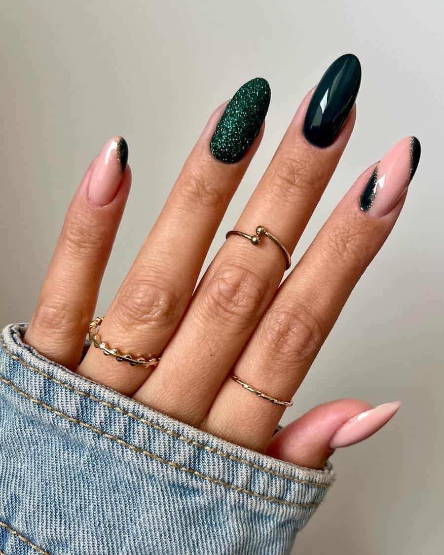 a hand with medium-length almond nails painted ɴuᴅᴇ and glossy dark green with sparkly forest green and gold glitter accents